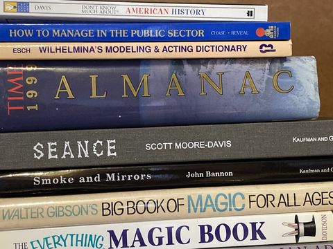 A stack of magic reference books, including an almanac and books on the history of magic tricks